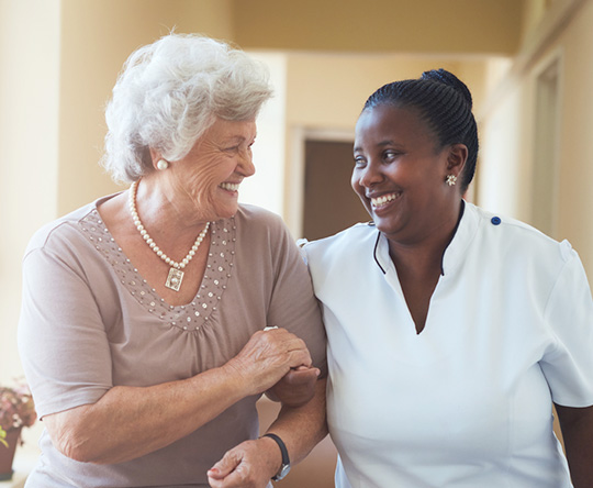 Caregiver arm in arm with senior woman walking down the hallway.
